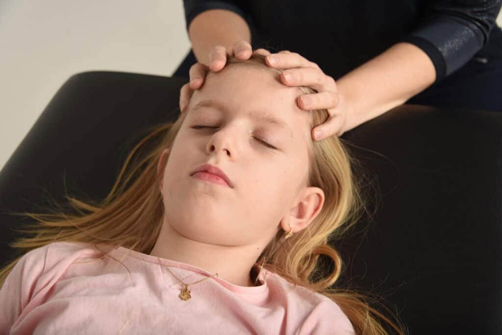Dívka ležící se zavřenýma očima. Zkouší kraniosakrální osteopatii.